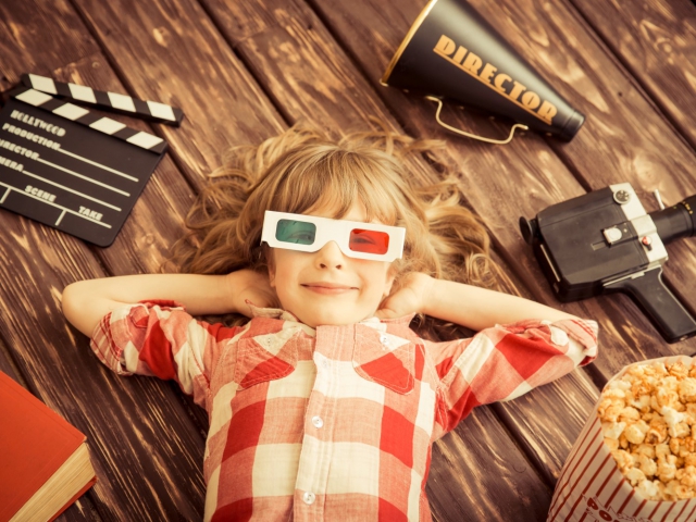 Jeune fille couché sur le dos au sol avec des lunettes 3D, autour d’elle clap de cinéma, caméra, pop-corn…