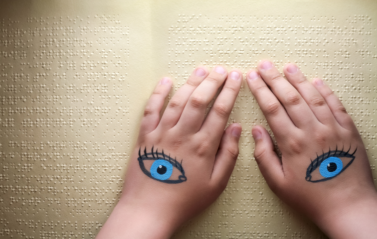 Image de deux mains posée sur un texte en braille, avec deux yeux peints aux dos des mains