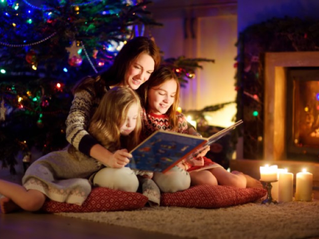 maman au pied d'un sapin de noël lisant une histoire à ses enfants