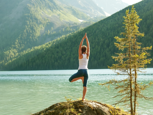 Femme en posture de yoga de l'arbre au bord d'un étang