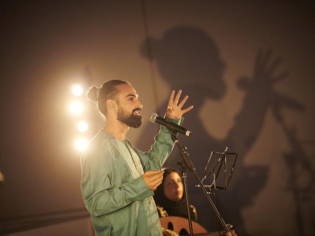 photographie de Rohan Houssein, debout devant un micro, en plein slam poésie