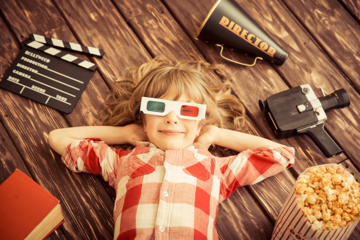 Jeune fille couché sur le dos au sol avec des lunettes 3D, autour d’elle clap de cinéma, caméra, pop-corn…