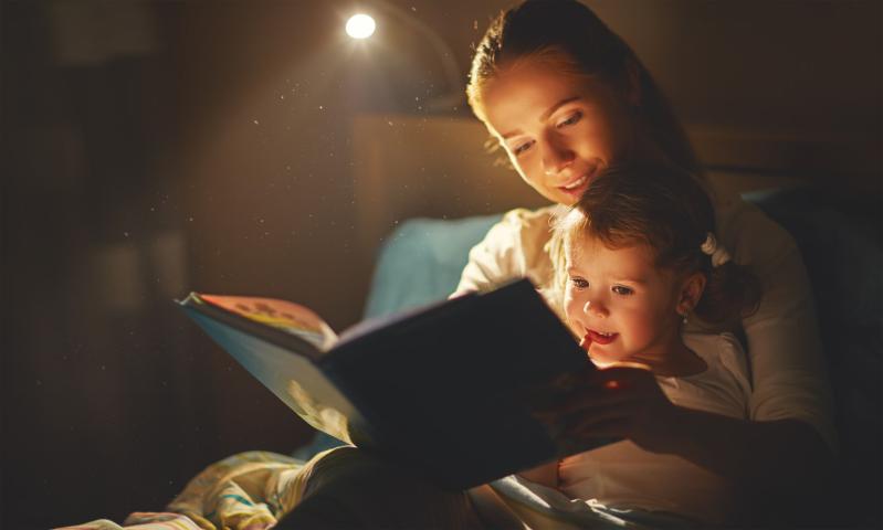 photographie d'une mère au lit avec son enfant entre les jambes, le livre devant l'enfant